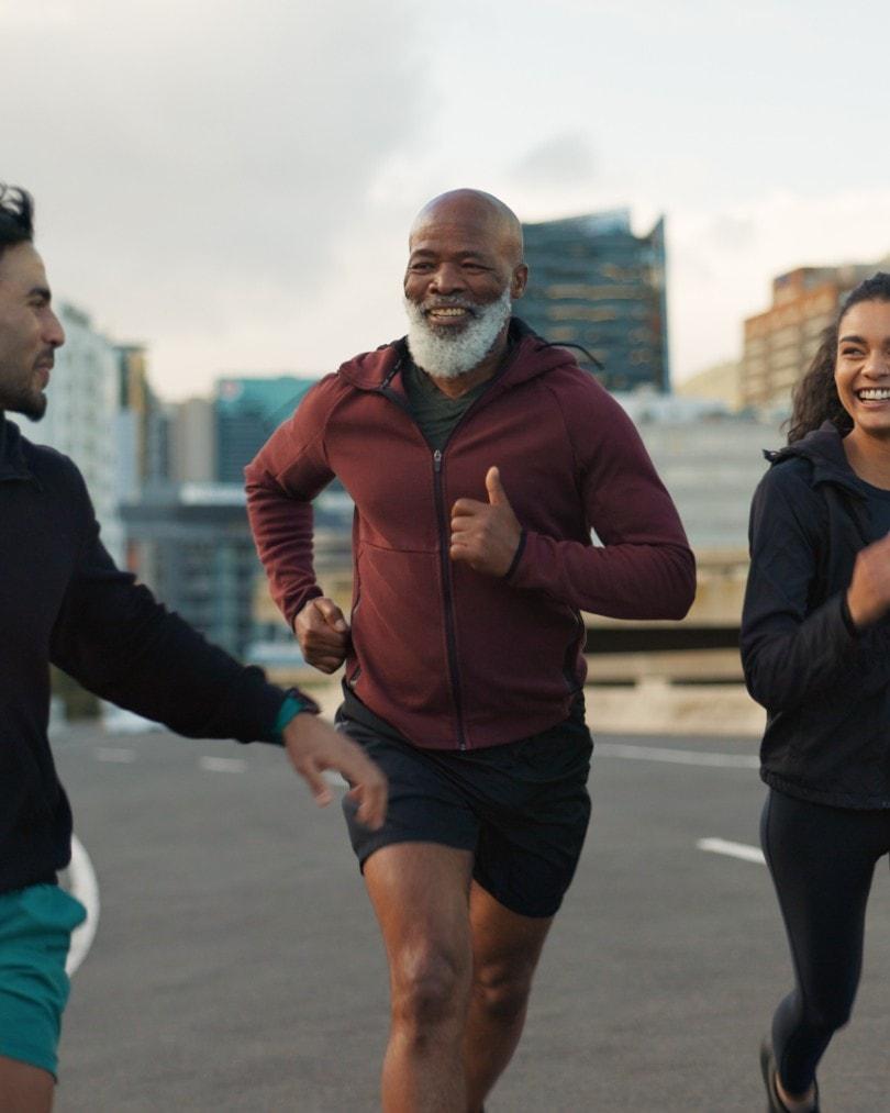A man in his fifties with a white beard, smiling while running through the city with friends
