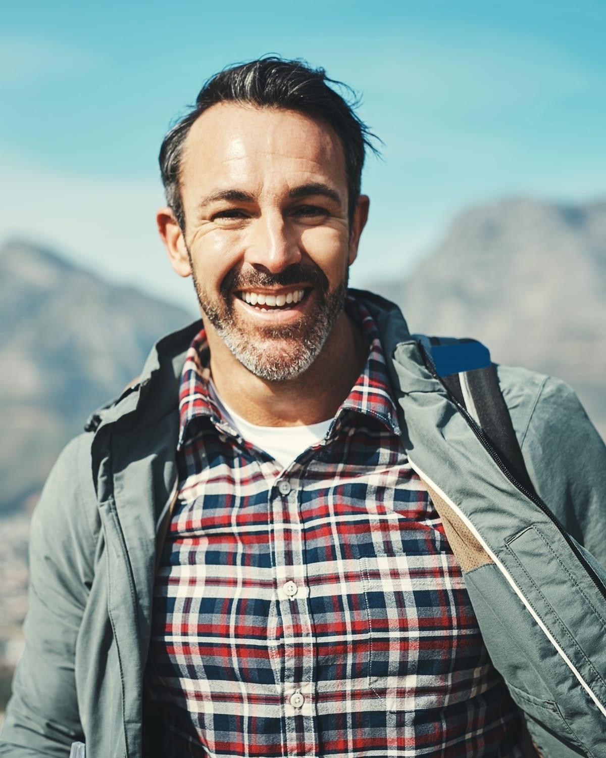 A man in his forties grinning on a mountain trail