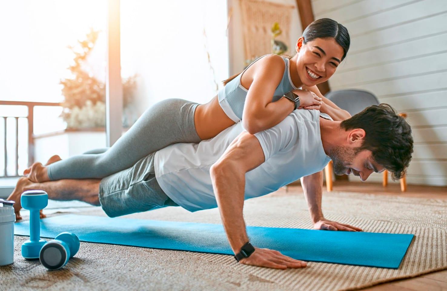 A man doing push-ups at home while his partner laughs on his back