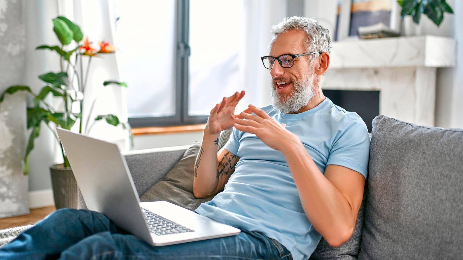A man on his sofa talking with his provider on a laptop video visit