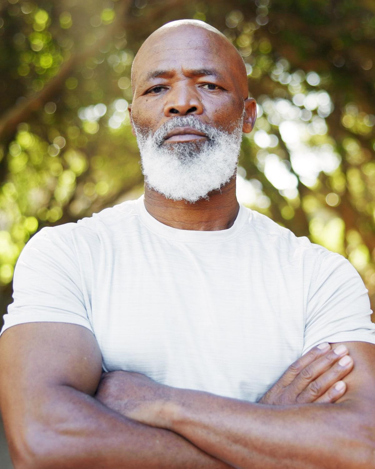 A man in his fifties with a white beard, arms folded, standing outdoors